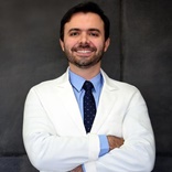 Dr Eduardo Alvares de braços cruzados, jaleco e gravata, sorrindo para a câmera